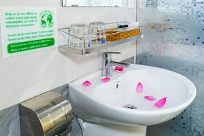A bathroom with a sink, a glass rack with toiletries, and a sign promoting water conservation. - The Rice Hotel&Tour - 39 Nguyen Trai No4 (Thanh pho Ho Chi Minh)
