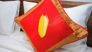 Una cama con ropa de cama blanca y una sola almohada roja con ribete dorado.