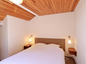 A bedroom with a wooden ceiling, a bed with a headboard, bedside tables, and wall-mounted lamps.