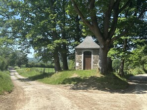 A rural road leading to a stone building with a pitched roof, surrounded by trees and greenery. - Pretty group house with a sauna, games & garden (Lierneux)