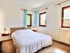 A bedroom with a bed, two bedside tables with lamps, a window with curtains, and a radiator.