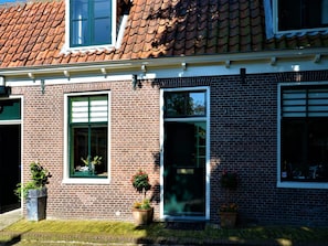 A two-story brick building with a tiled roof, large windows, and potted plants. - Authentic fisherman's house in the heart of Edam (Edam)
