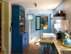 A kitchen with blue cabinets, a window with blinds, a sink, and a kettle. - Authentic fisherman's house in the heart of Edam (Edam)
