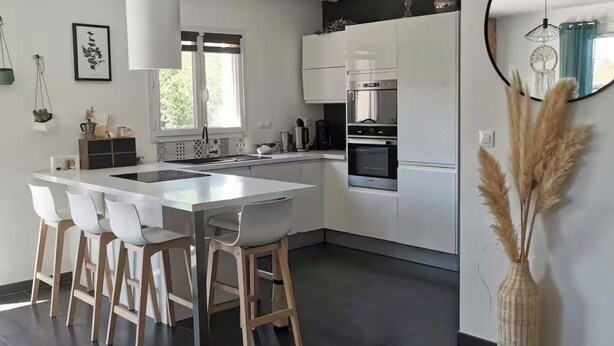 Ett modernt kök med en central köksö, barstolar, ett stort fönster och en dekorativ vas.