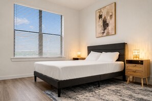 Une chambre à coucher avec un lit, des tables de chevet, une commode, une fenêtre avec des stores et un tableau au mur.