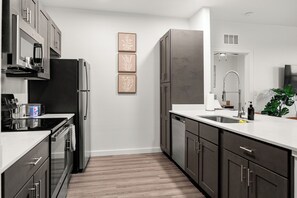 Une cuisine moderne dotée d’appareils électroménagers en acier inoxydable, d’un plan de travail blanc et d’un plancher en bois.