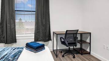 Una habitación con cama, escritorio con silla, ventana con cortinas y vista al exterior.