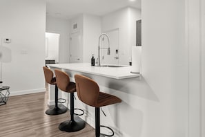 Eine moderne Küche mit weißer Arbeitsplatte, einem schwarzen Wasserhahn und braunen Barhocker.