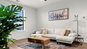 En moderne stue med en hvid sofa, et træ sofabord, et bybillede som billede og en gulvlampe.