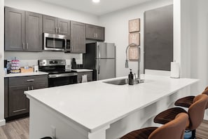A modern kitchen with dark cabinets, stainless steel appliances, a white countertop, and a bar seating area.