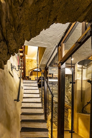 Eine Wendeltreppe mit Steinwänden und einer Glaseinfassung, die zu einem Badezimmer mit Dusche führt.