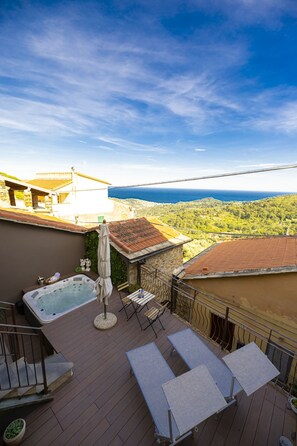 Eine Dachterrasse mit Whirlpool, Liegestühlen und Blick aufs Meer.