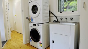 Une buanderie équipée de machines à laver superposées, d’un sèche-linge et d’une fenêtre donnant sur un espace verdoyant.