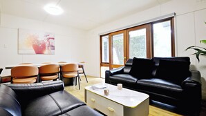 Un salon moderne avec un canapé en cuir noir, une table basse blanche et un coin repas comprenant des chaises et une table en bois.