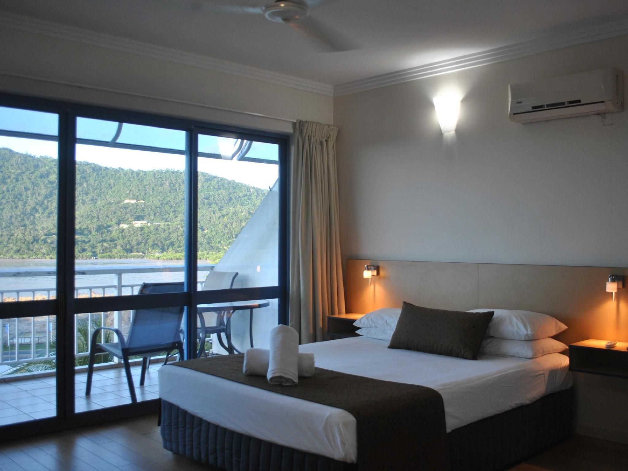 Habitación de hotel con cama, una silla, una mesa, un balcón con vistas a las montañas y un aire acondicionado en la pared.