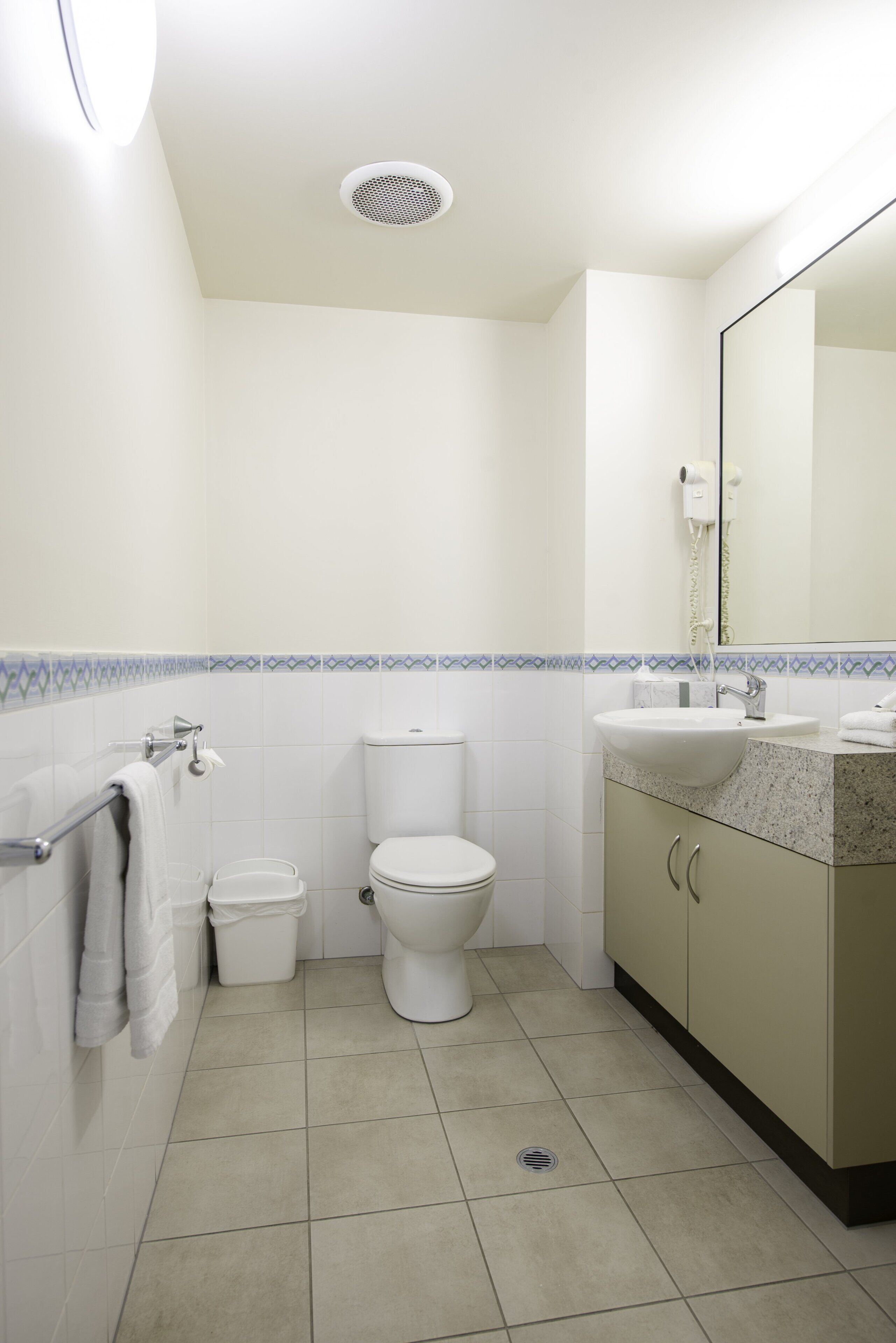 A bathroom with a toilet, sink, mirror, and tiled floor.