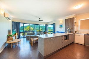A modern kitchen with a central island, large windows, and a view of greenery.