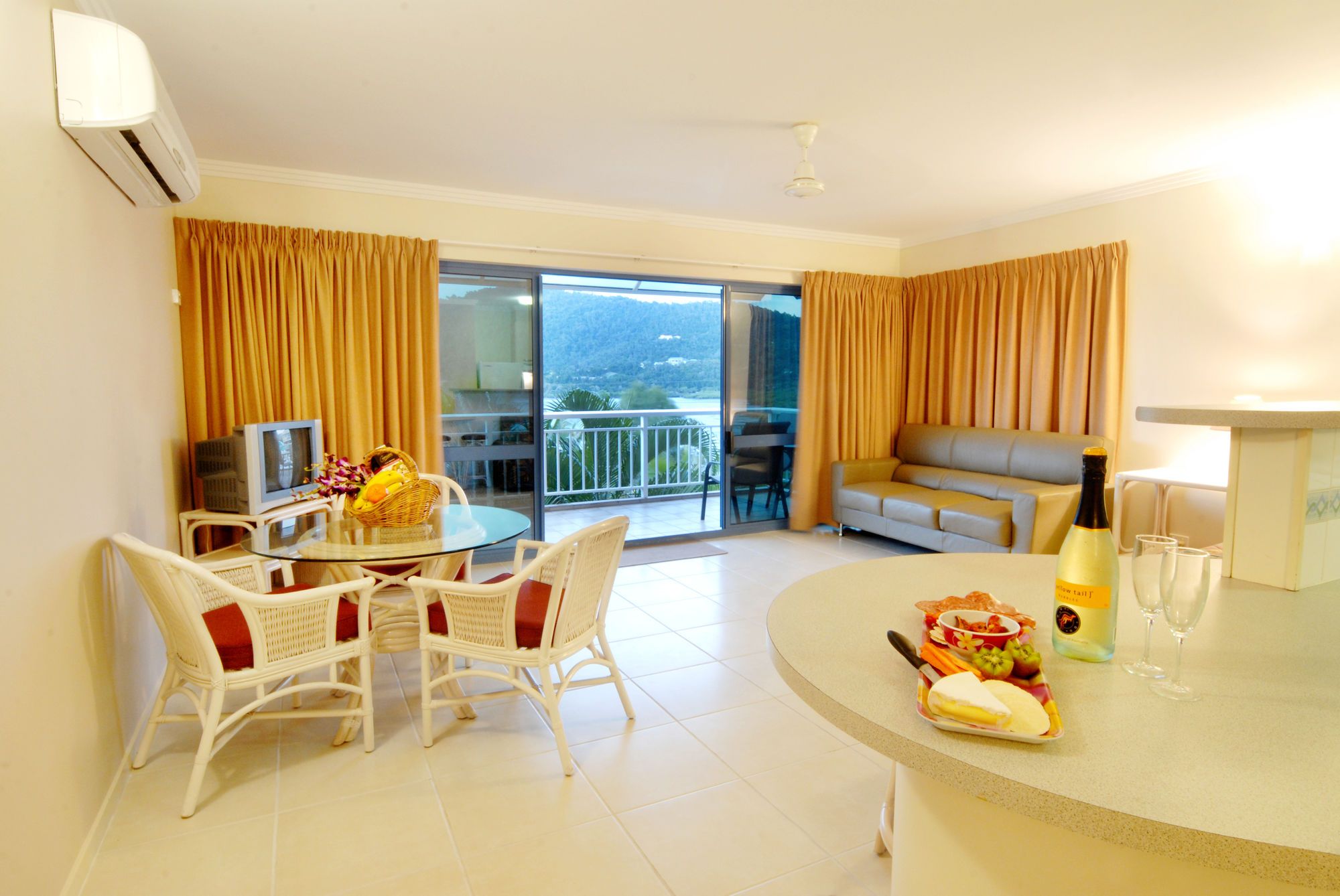 A hotel room with a balcony, a dining area with a table and chairs, a sofa, and a minibar.