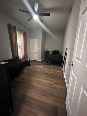 A bedroom with a bed, a desk, a ceiling fan, a door, and a window with curtains. - Spacious centrally located 4-bedroom house in charming Kansas City (Kansas City)