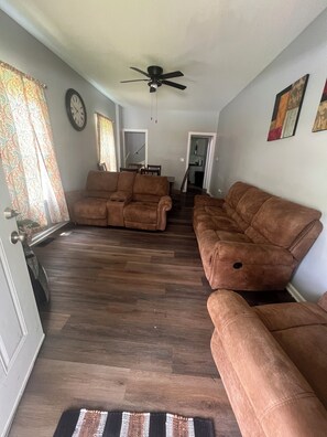 Ein Wohnzimmer mit zwei braunen Sofas, einem Deckenventilator, einer Uhr und einer Tür zu einem anderen Raum.