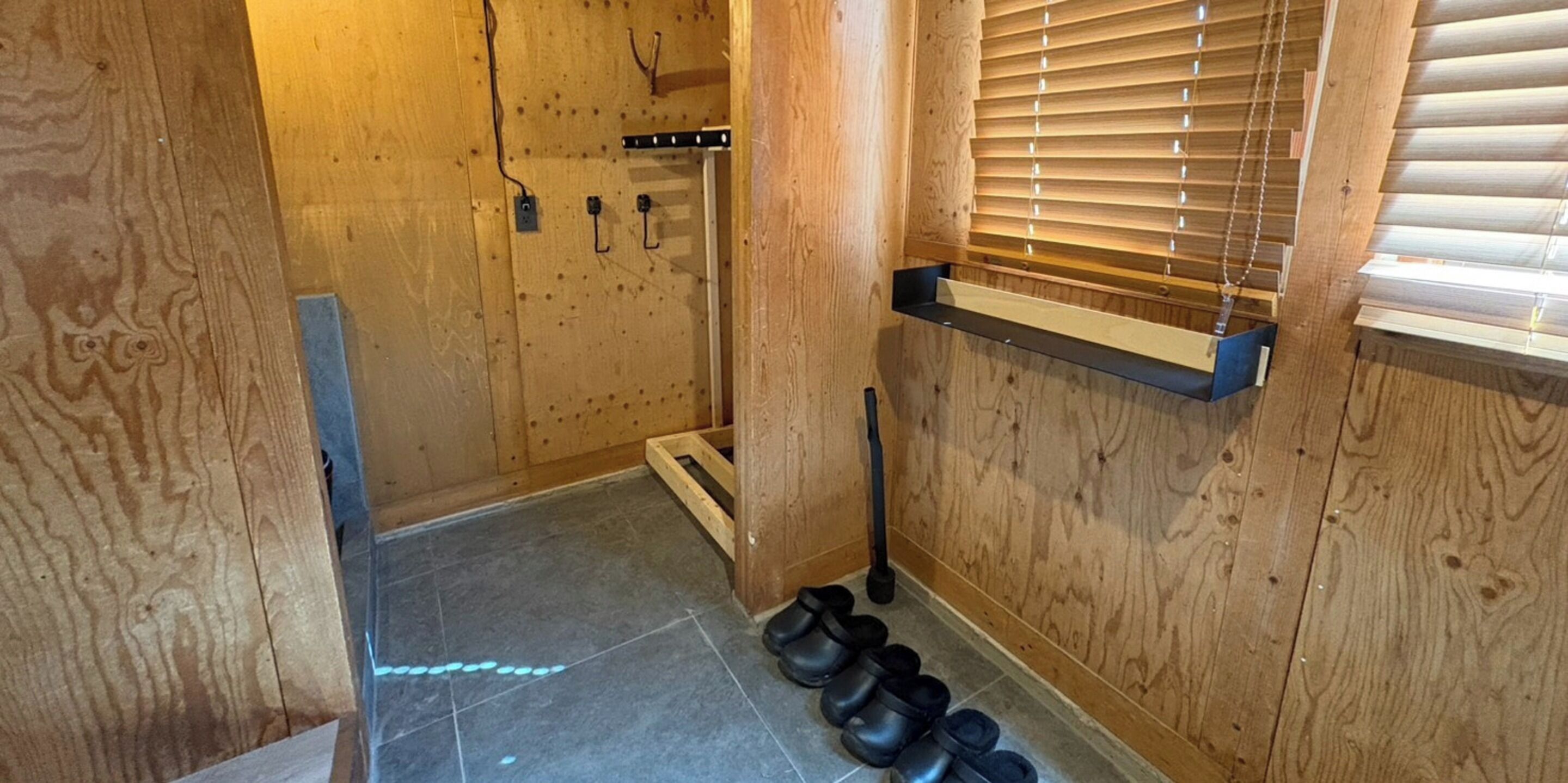 A wooden interior with a tiled floor, a wooden bench, and a pair of black shoes.