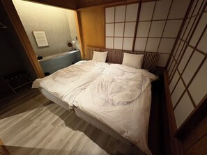 A bed with a white comforter, a wooden headboard, and a small bedside table with a mirror. - REN HANARE Hakuba (Hakuba)