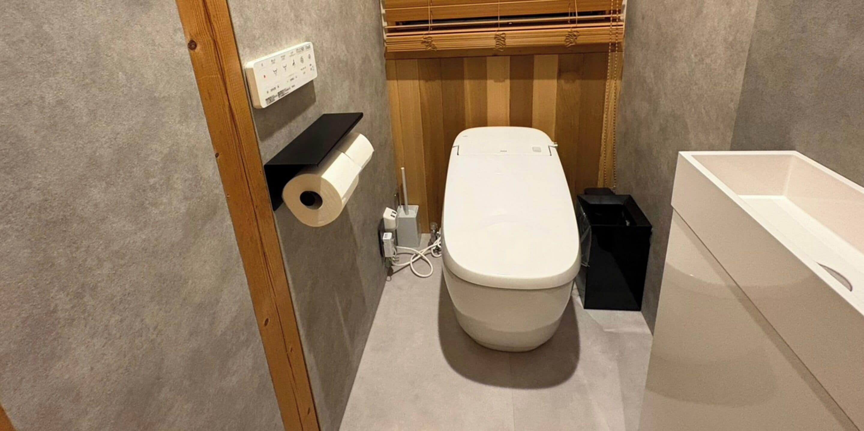 A small bathroom with a toilet, a roll of toilet paper, a black trash bin, and a white bathtub.