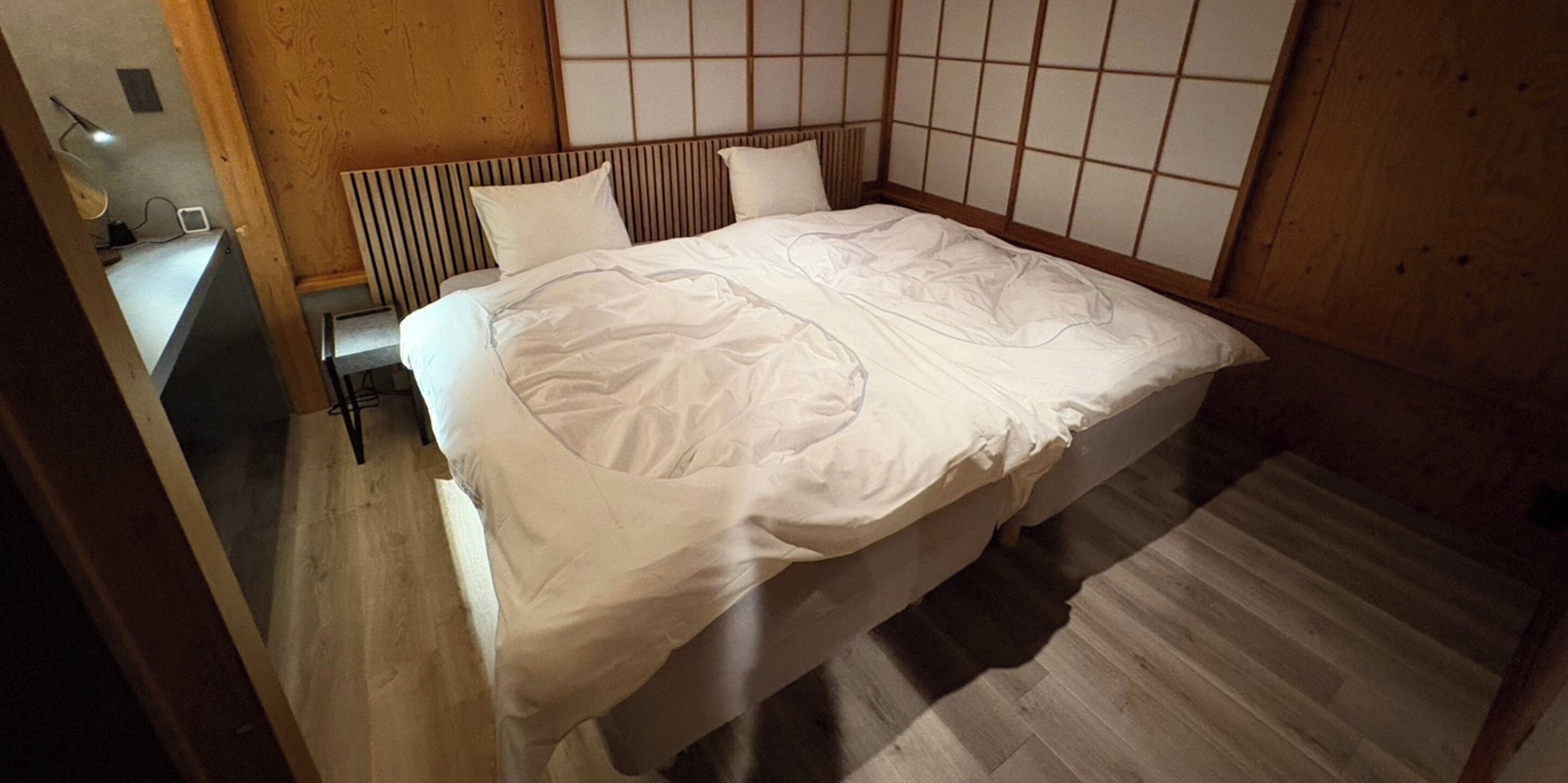 A neatly made bed in a room with a wooden headboard, a small bedside table, and a light fixture on the wall.