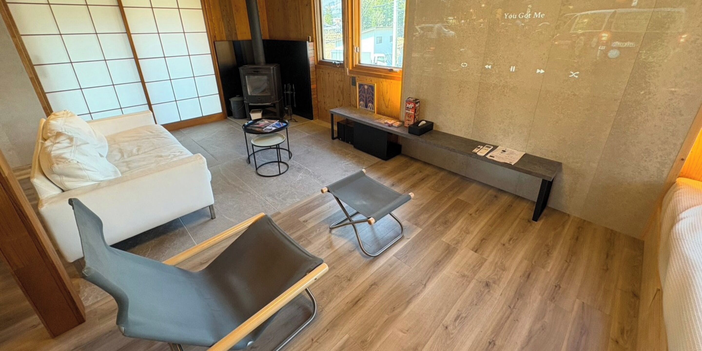 A modern living room with a sofa, a black chair, a small table, a fireplace, and a window with a view.