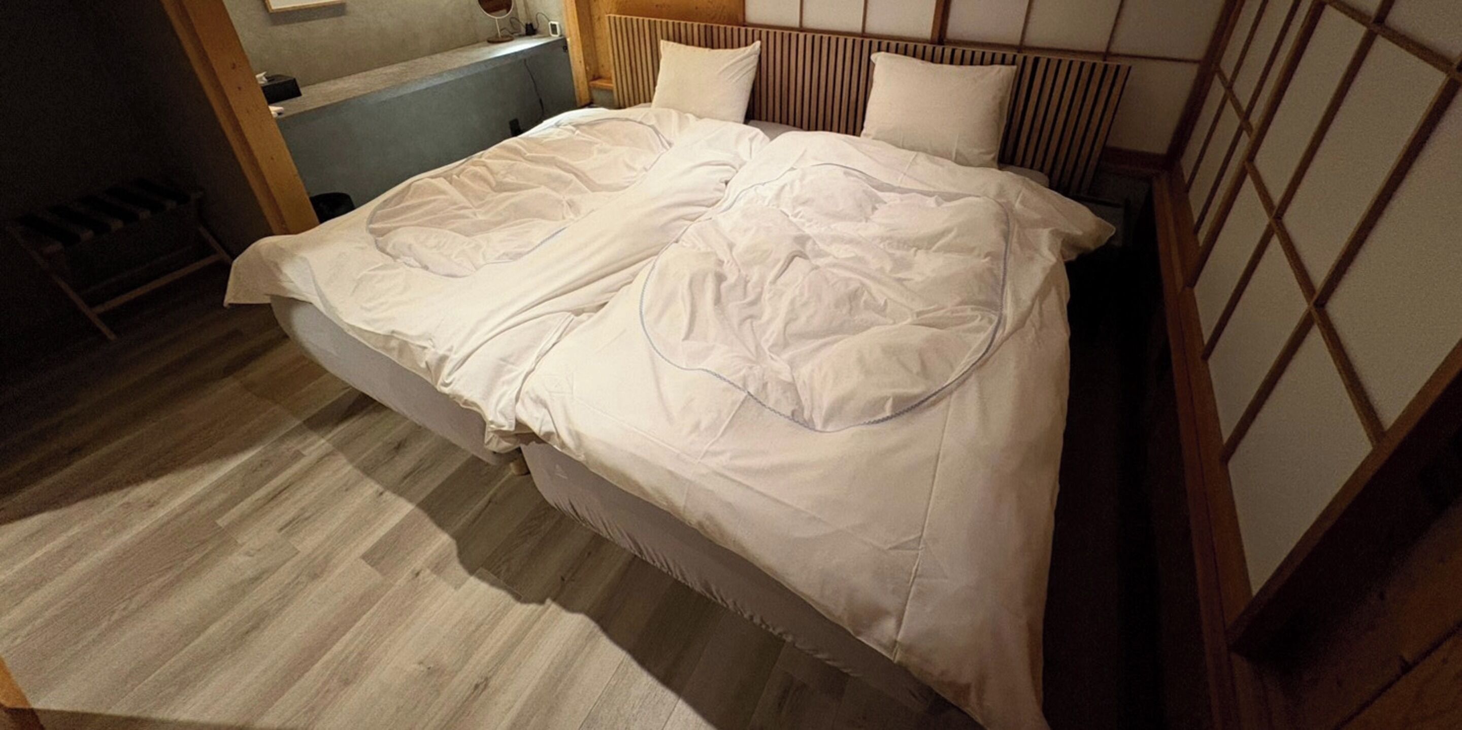 A bed with white bedding, a wooden headboard, and a wooden floor.