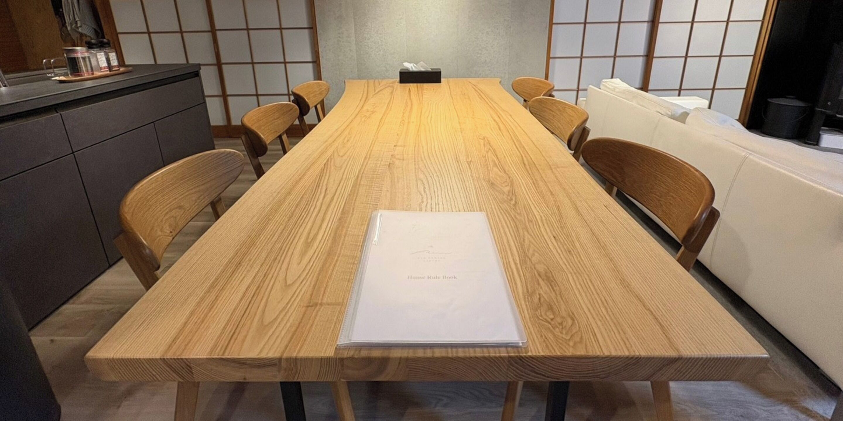 A conference room with a long wooden table, six chairs, a whiteboard, and a small cabinet with a kettle.