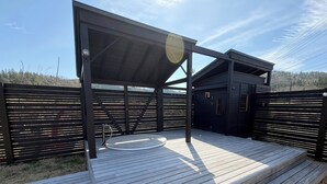 A covered outdoor deck with a circular seating area, a small building, and a fence. - REN HANARE Hakuba (Hakuba)