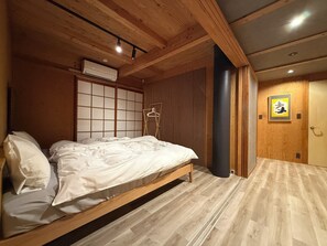 A bedroom with a wooden bed, a hanging clothes rack, a sliding door, and a wall-mounted air conditioner. - REN HANARE Hakuba (Hakuba)