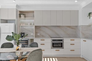 Una cocina moderna con armarios blancos, un protector contra salpicaduras de mármol y un horno empotrado.