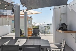 Un patio al aire libre con una mesa, sillas, una parrilla y sombrillas que dan sombra.