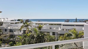 Una zona residenziale costiera con edifici bianchi moderni, palme e una vista chiara sull'oceano.