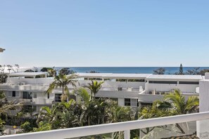 Zona residencial costera con edificios blancos modernos, palmeras y una vista despejada del océano.