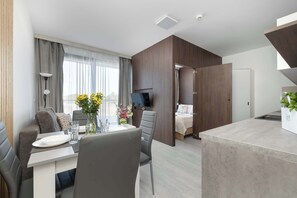 Una habitación de hotel moderna con comedor, televisión, cama y kitchenette.