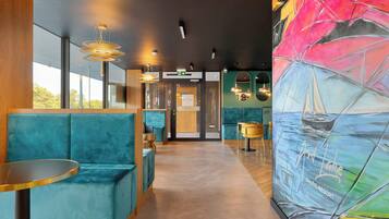 Un intérieur moderne avec des sièges de couleur turquoise, une fresque représentant un voilier et un comptoir d’accueil en bois.