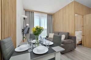 Ein modernes Zimmer mit Esstisch für zwei Personen, einer Couch, einem Fernseher und einem Kleiderschrank.