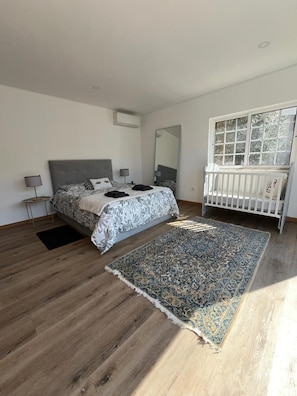 A bedroom with a bed, bedside tables, a crib, a large mirror, and a window.