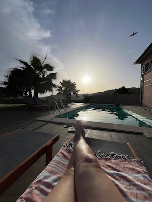 A poolside view with a reclining chair, palm trees, and a clear sky.
