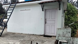 A white building with a door, a concrete floor, and a ladder. - Woodcock Cottage (Ooty)