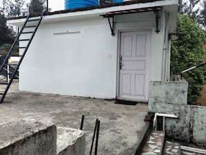 A white building with a door, a concrete floor, and a ladder. - Woodcock Cottage (Ooty)