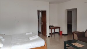 A room with a bed, a coffee table, a sofa, a small table with a red bucket, and a door leading to another room. - Woodcock Cottage (Ooty)