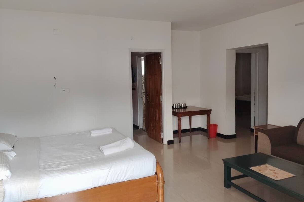 Una habitación con una cama, una mesita de centro, un sofá, una pequeña mesa con un cubo rojo y una puerta que da a otra habitación.