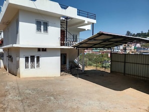 A two-story building with a balcony, a covered outdoor area, and a view of the surrounding neighborhood. - Woodcock Cottage (Ooty)