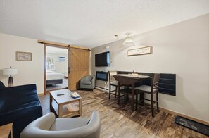 Ein kleines Hotelzimmer mit Bett, Schreibtisch, Stuhl, Fernseher und Essecke.