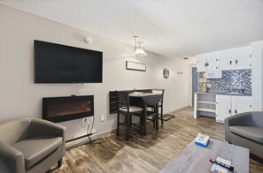 Ein Wohnzimmer mit Flachbildfernseher, ein Essbereich mit Tisch und Stühlen, eine Küche mit weißen Schränken und einem Deckenventilator.