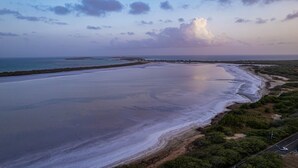 A coastal landscape with a wide beach, a road parallel to the shore, and distant buildings. - Cozy Camper w/Pool · Cabo Rojo Lighthouse ·Combate (Boquerón)